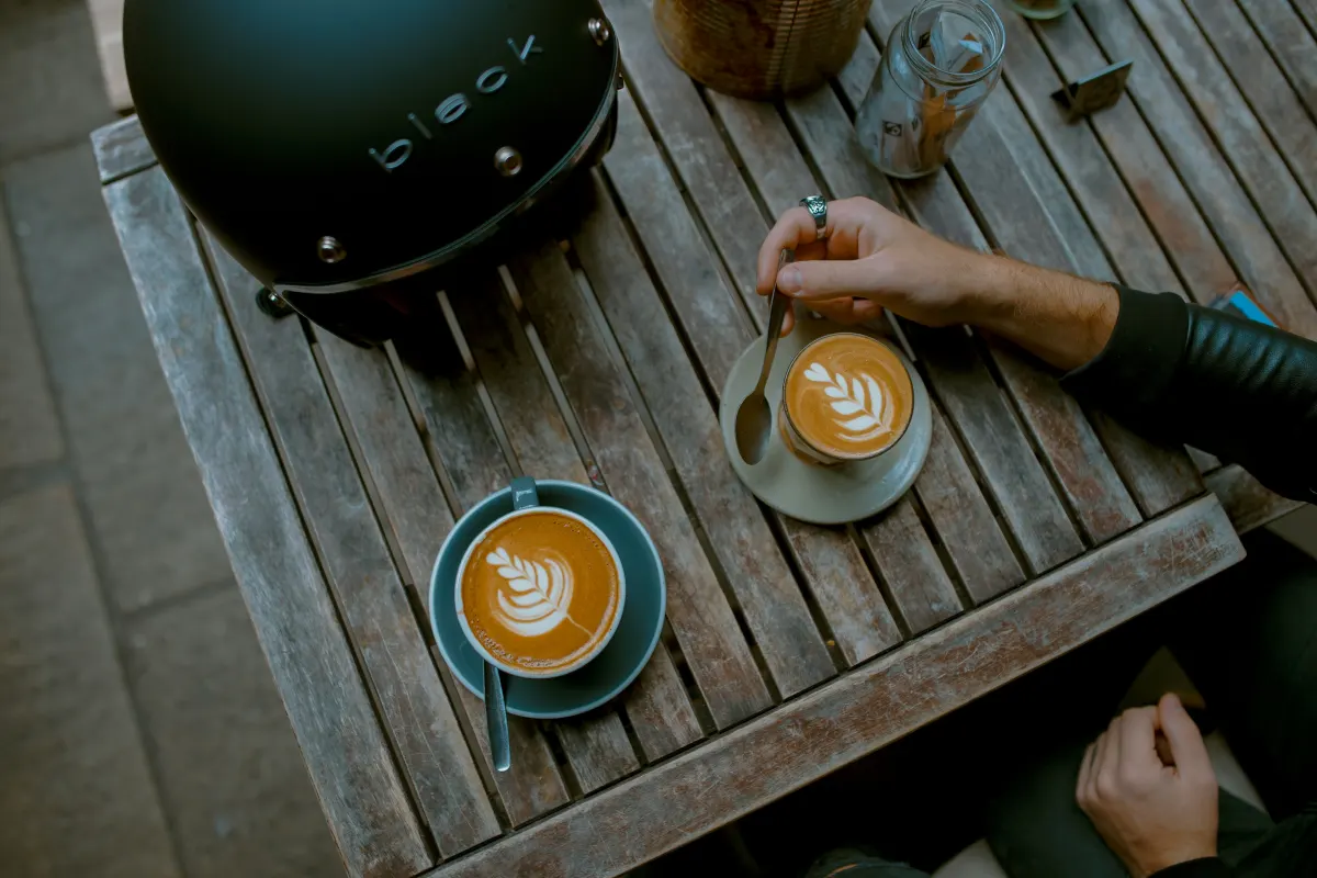 Two coffees on a café table beside a helmet